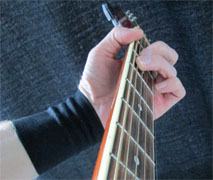 Hand som håller gitarrhals med armband kring handled